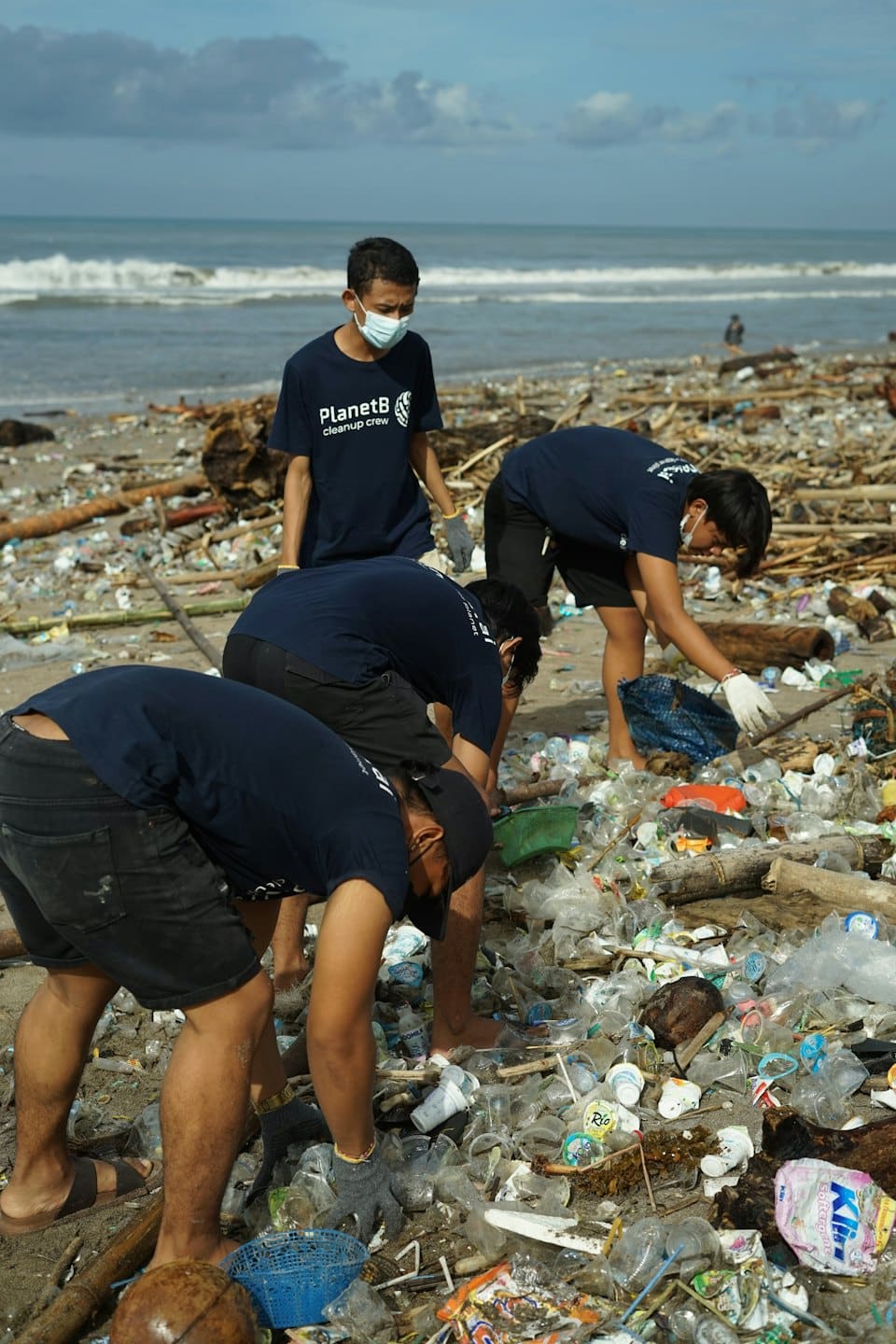 People in PlanetB cleanup crew shirts collecting plastic from a beach.