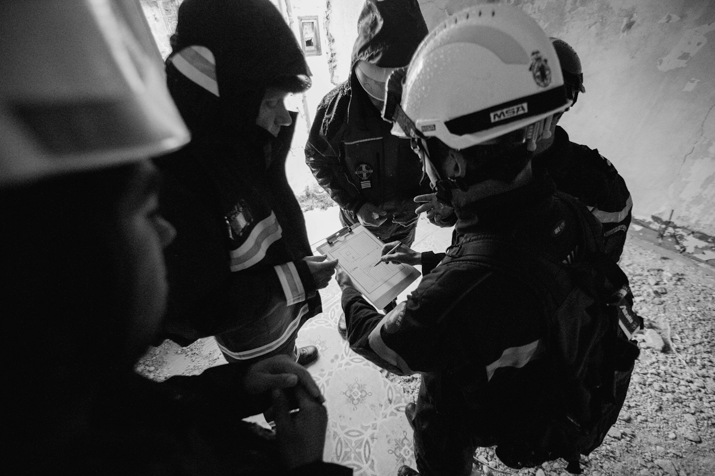 Four workers in hard hats review a floor plan at a construction site.
