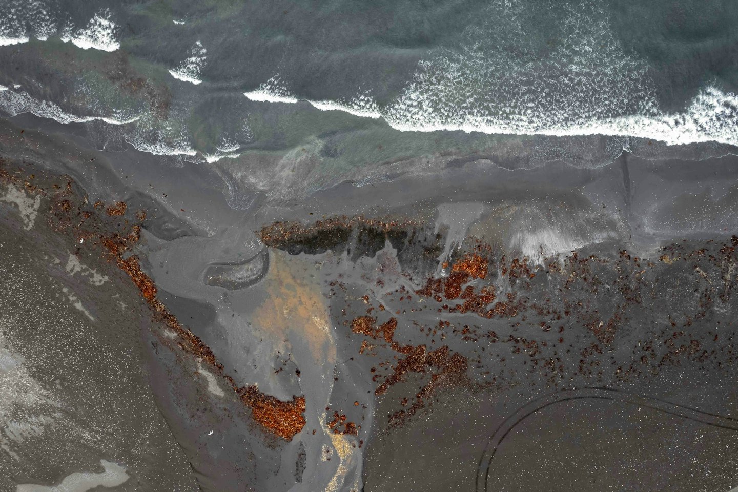 Waves crash against the dark volcanic sand beach.