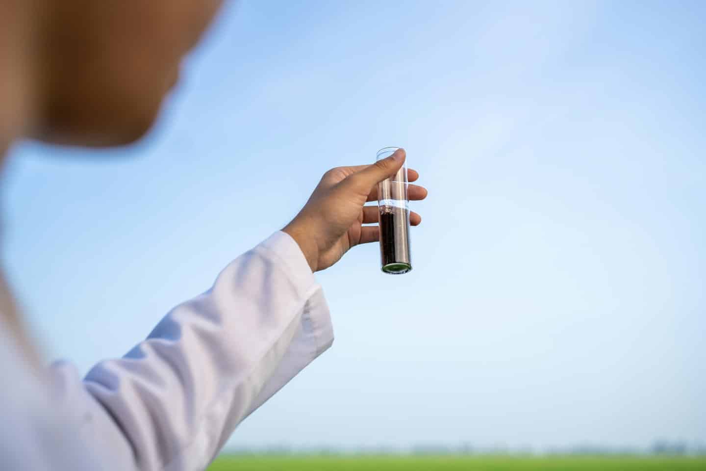 Scientist examines soil sample in test tube outdoors.